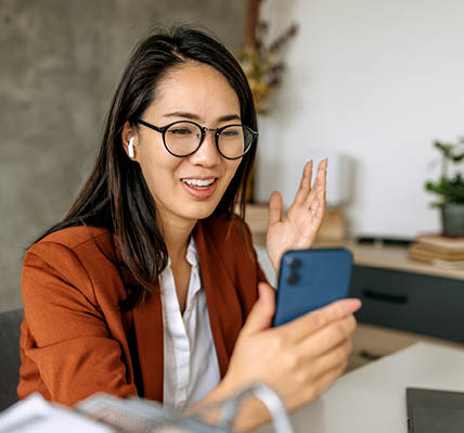 A businesswoman, using her smartphone and wireless earbuds having productive video call while working from her home office
