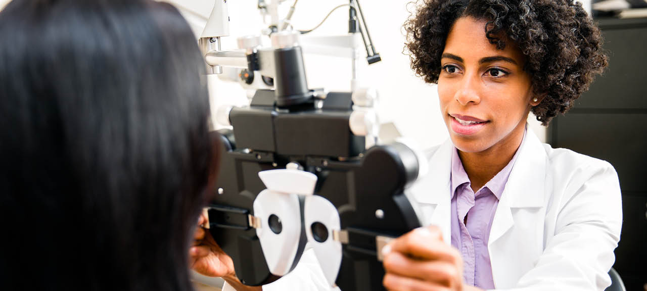 A African American optometrist is checking her patient's eye sight. Optometrist is ethnic of African Decent. Doctor is in ethnic minority. She is checking her patient's eye sight by pulling eye test equipment - Phoropter. Its real optometrist office.   