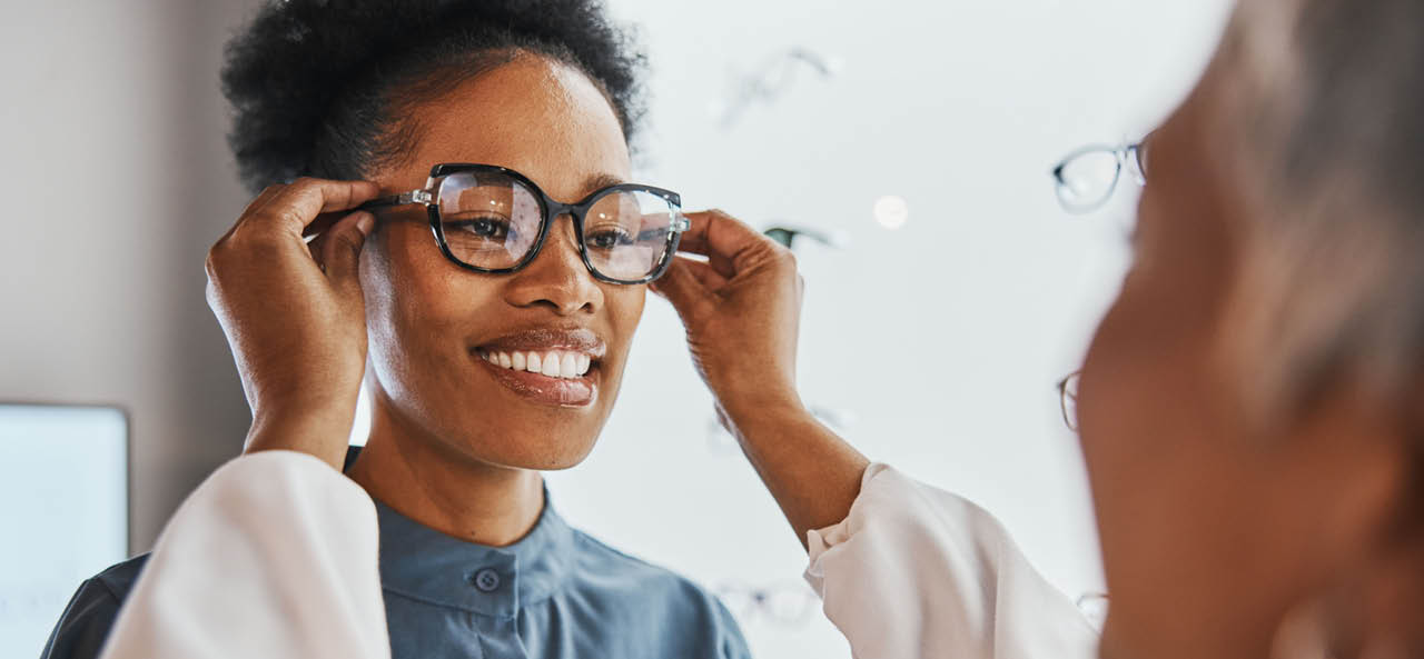 Glasses check, black woman and customer with store worker and optician looking at lense. Eye consulting, smile and eyewear assessment in a frame shop for vision test and prescription exam for eyes