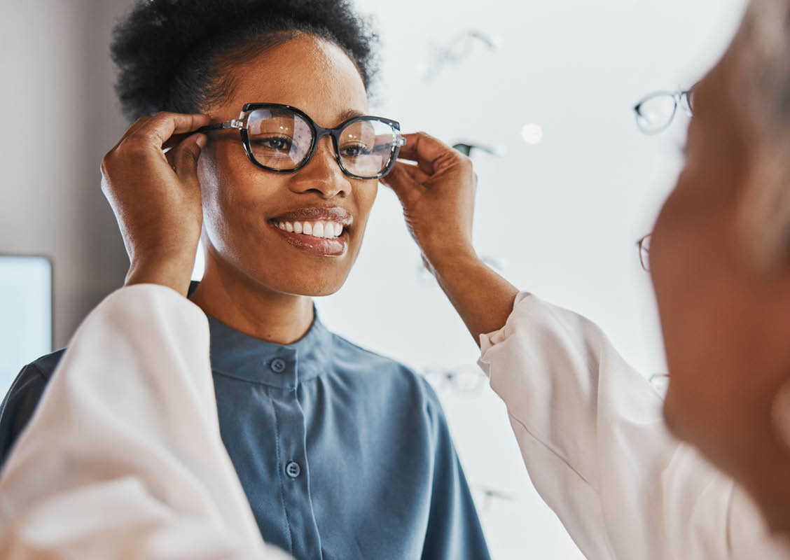 Glasses check, black woman and customer with store worker and optician looking at lense. Eye consulting, smile and eyewear assessment in a frame shop for vision test and prescription exam for eyes