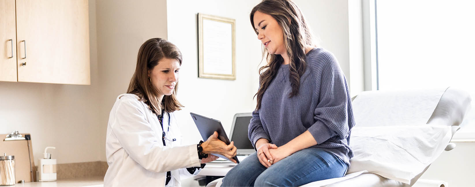 Female doctor discussing treatment on digital tablet with female patient in exam room