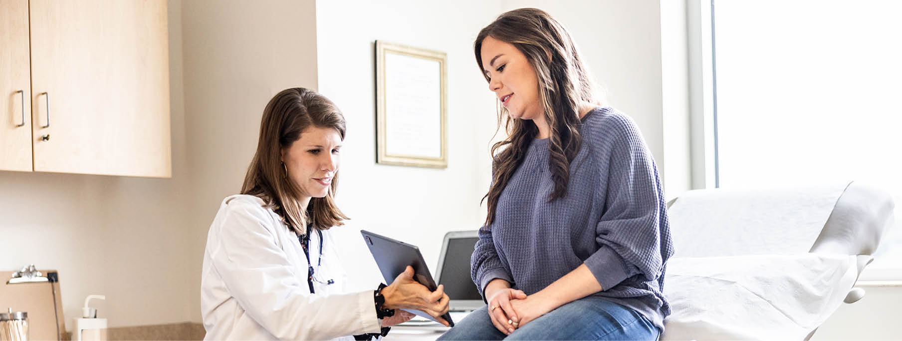 Female doctor discussing treatment on digital tablet with female patient in exam room