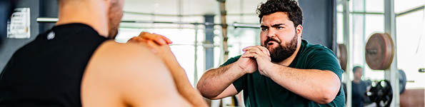 Mid adult man doing squats with personal trainer at gym