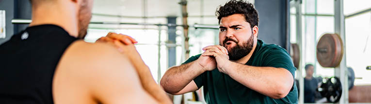 Mid adult man doing squats with personal trainer at gym