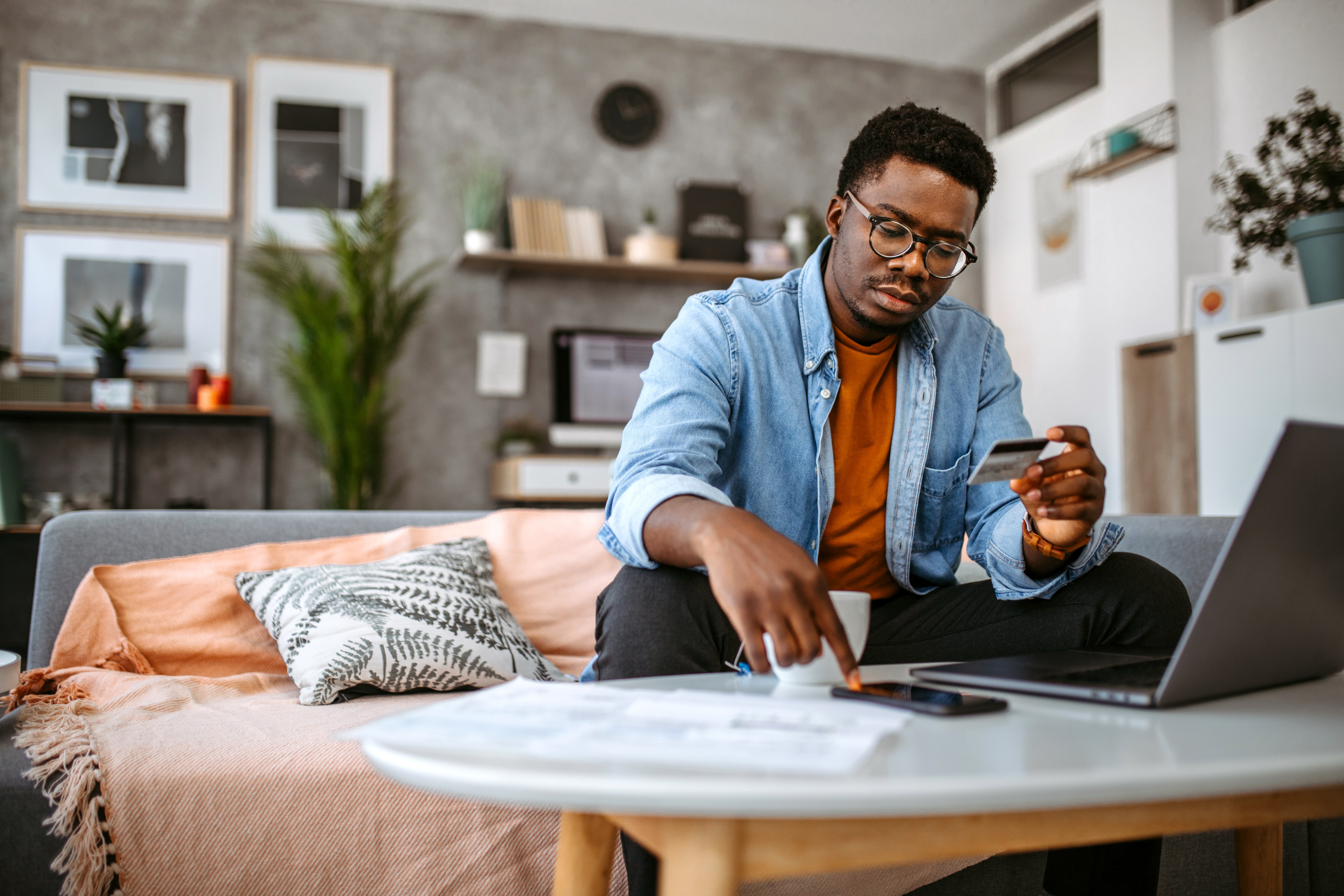 Man examines credit card in front of laptop screen. 