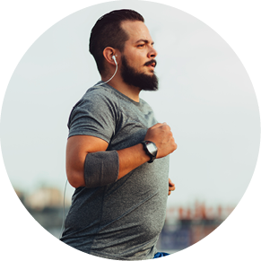 Urban hipster man running in the city. He is listening music and trying to get fit. Buildings in background. Wearing modern sports clothes.