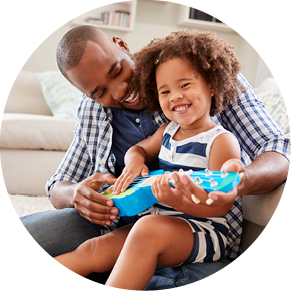 Toddler daughter sits on dad s knee playing ukulele at home